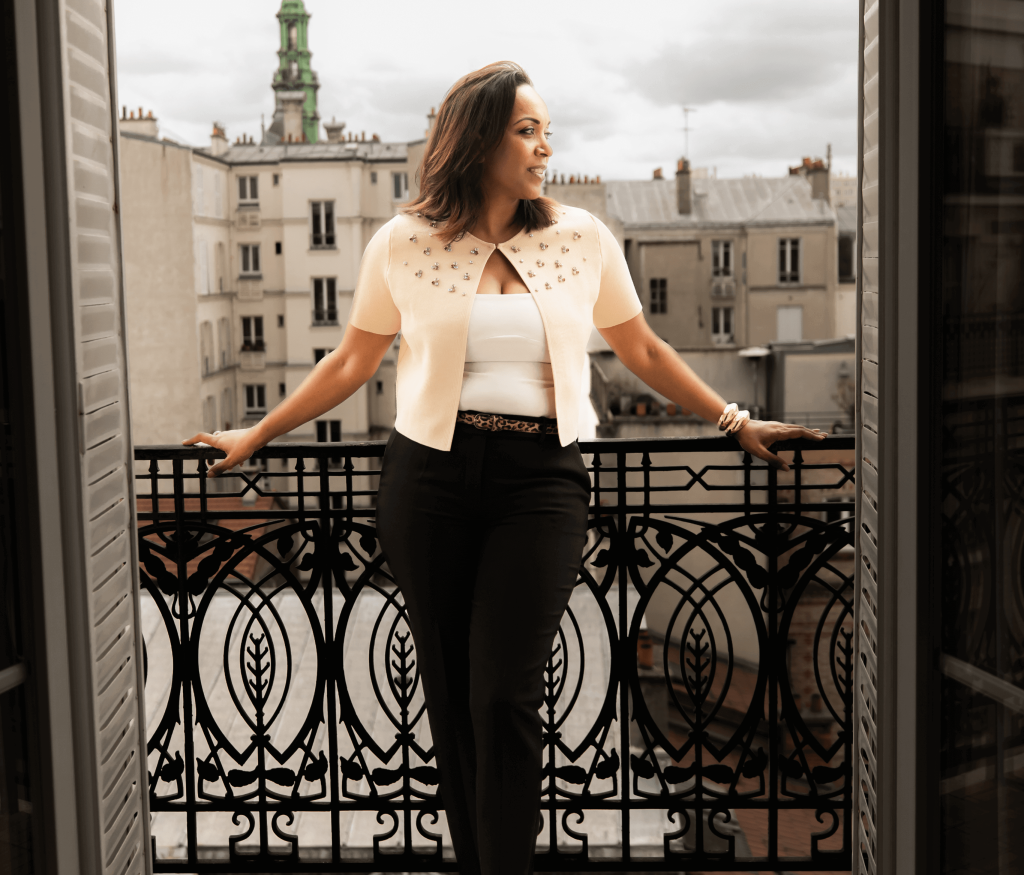 Une femme sur un balcon, observant la ville avec ses bâtiments et rues en contrebas.
